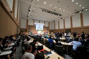 People in a conference hall, listening to a speaker at the podium