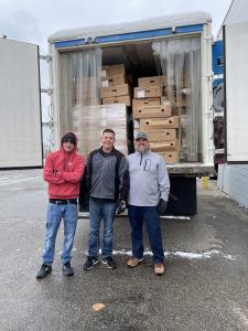Three men standing in front of a refrigerated truck full of frozen turkeys.