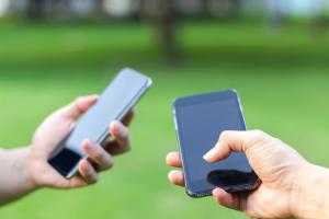 Two people holding cell phones with grass in the background.