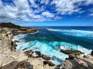 Vivid blue waters crash against rugged cliffs at Po'ipu Beach, framed by a bright, cloud-streaked sky.