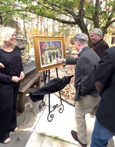 Ann Bailey smiling with her live event portrait painting on easel, as the collectors look at it.