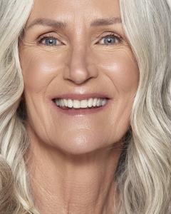 A slowing mature woman smiles into the lens, while showing her gorgeous skin.