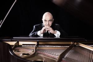 GRAMMY® Award winner Omar Akram seated in a dark room at a grand piano looking out across the strings
