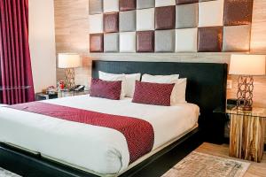 A cozy king room at the Catalina Hotel featuring a large bed with white linens and red accent pillows, an artistic padded headboard, elegant bedside lamps on glass nightstands, and rich maroon drapes.