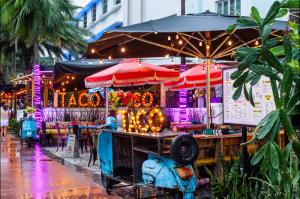 Colorful outdoor Taco Taco restaurant at the Catalina Hotel with neon signs, bright umbrellas, string lights, and a tropical backdrop, inviting guests for a lively dining experience.