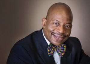 Dr. J. Keith Motley smiles for a headshot on a brown backdrop.