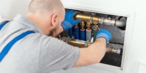 Man using tools on pipes under a sink.