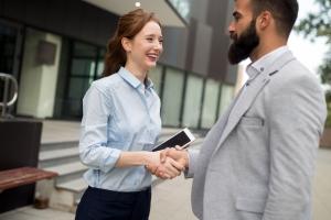 An executive personal assistant with a phone, smiling and shaking hands with her CEO employer outside his modern home or office