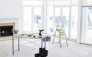 Room inside of a house under construction with tools, a fireplace, open windows, and a ladder.