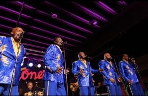 The Temptations Review featuring the legacy of Dennis Edwards performing on stage in turquoise suits.