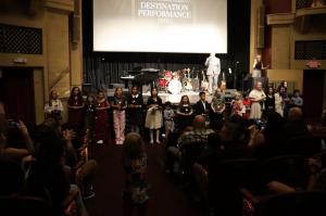 Children on stage at The Strand Theatre in Marietta, dressed in performance attire, with a backdrop announcing 'Destination Performance Series' and audience members taking photos.