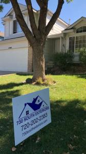 A picture of a roofing yard sign in the grass in front a roof that was completed