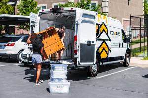 White Kingbee Daily Rental van with Kingbee wrap on the van and two women loading a dresser into the the back of the van.