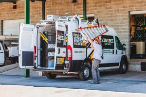 White Kingbee Daily Rental van with Kingbee wrap on the van and a contractor loading a ladder onto a roof ladder rack.