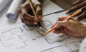 Two people holding pencils with a blueprint of a home.