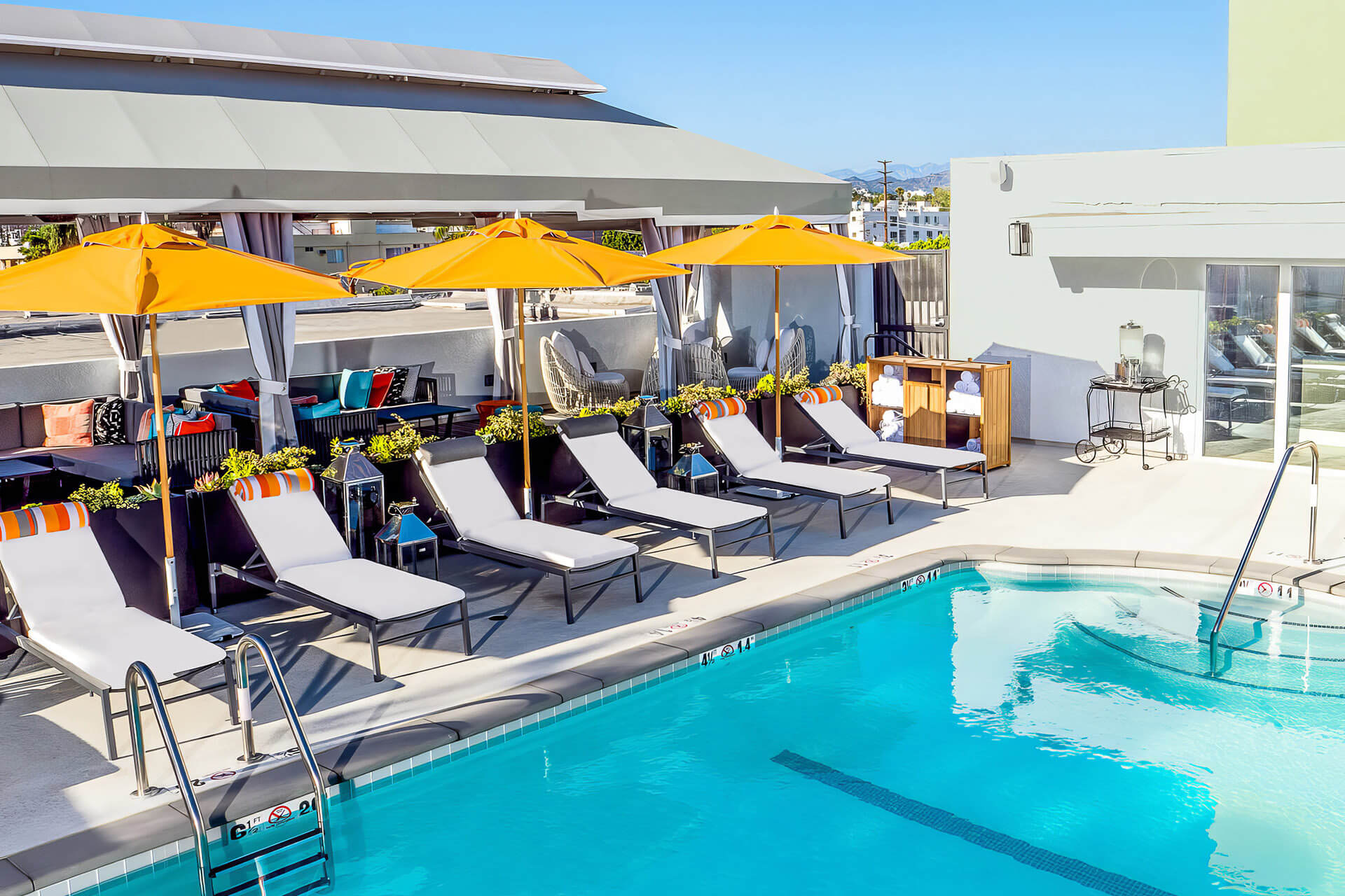 Rooftop swimming pool at Le Parc Melrose with lounge chairs and orange umbrellas, overlooking panoramic views of West Hollywood.