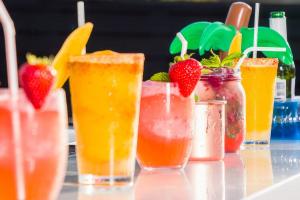 A vibrant array of colorful cocktails adorned with fresh fruit garnishes, glistening in the sunlight on a bar top.