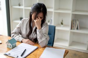 A stressed and upset Asian female real estate agent is sitting at her desk in the office