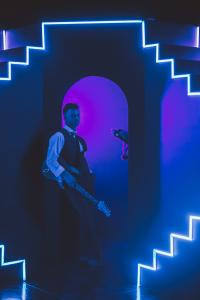 Dylan Galvin posing with his guitar with the blue puppet cat Munch for the filming the music video for his music video How to Write a Pop Song