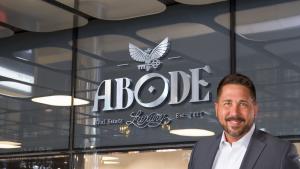 The founder and CEO of ABODE, standing confidently in front of the ABODE logo signage at the grand entrance of the new Nashville location. A symbol of leadership and commitment to excellence, they herald the provision of luxury real estate services tailor