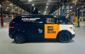 Side view of a new Canoo electric vehicle wrapped in black, white and yellow with
