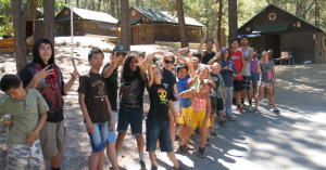 Children at Jay Nolan Camp smiling and posing for a group photo in front of their cabins.