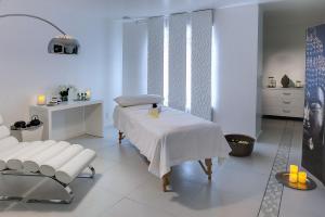 A modern spa room with a massage table, white lounging chair, ambient candles, and a decor of peaceful Buddha imagery, promoting a relaxing atmosphere.