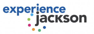 Logo with the text 'experience jackson' in mixed blue and black lowercase letters. Above the letter 'i' in 'experience' and surrounding the text are nine dots in a variety of colors including light blue, orange, dark blue, green, and pink, resembling a pl