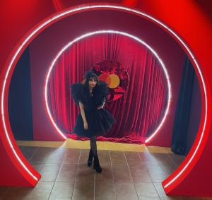 Glamorous young lady in black couture dress and spectator hat posing inside a red circle.