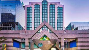  A glass and metal high-rise hotel with a green awning and a large sign in front of it.