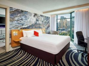 Modern hotel room with a king-size bed, stylish furnishings, and a large window overlooking a city view.