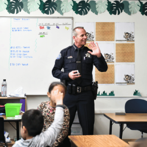 A police officer interacting with students, in front of a classroom.