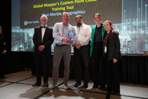 Blue Marble Geographics team stands on a stage smiling with the award and host. Mike Childs is holding the award.