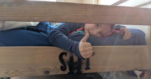 Boy peeking through the footboard of his new bed giving a thumbs up