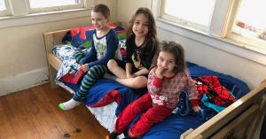 3 kids sitting on a bed smiling
