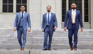 A photograph depicts three men in formal blue suits, each sporting a serious expression and a beard, walking down the steps of the courthouse's main entrance in Miami