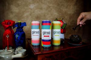 three beverage cans in a traditional Korean setting with ginseng extract dripping from spoon