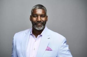 Headshot of Paul Francisco. He wears a light blue suit and stands in front of a gray background.