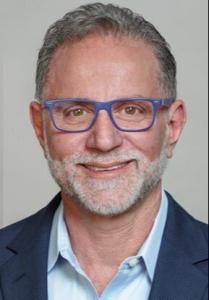 A professional headshot of Dean Rouso, the SVP of Innovation at Baird & Warner, wearing a blue suit, collared shirt and blue-framed glasses.