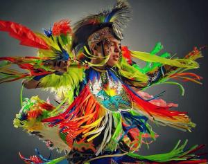 A young Native American man dances in a colorful indigenous outfit