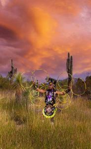 A adolescent Native American boy poses in formation while hoop in full regalia dancing outside in the desert
