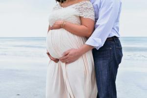 Pregnant male and female couple on beach with focus on her pregnant tummy