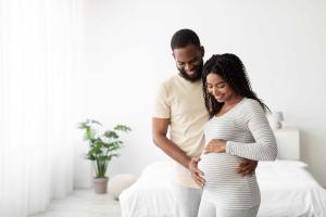Couple standing in white room with both of their focus on her pregnant belly.