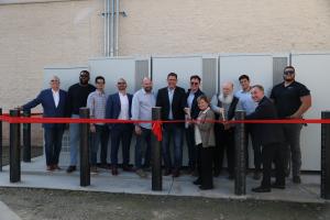 Members of the project team are standing in front of the battery energy storage system about to cut a red ribbon.