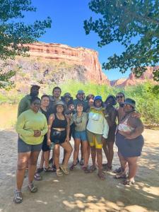 A group of guests pose for a photo while at a desert campsite with the river in the background.