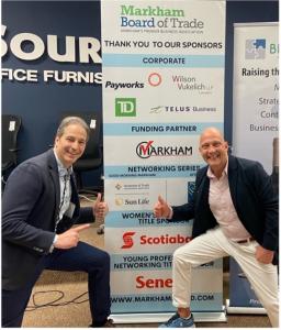 Photo of Andy Kovacs, President of Moments of Truth Insurance Services, and Chris Collucci, President & CEO of the Markham Board of Trade, standing side by side in front of a MBT Sponsor banner. Both men are smiling giving a thumbs up and appear engaged, 