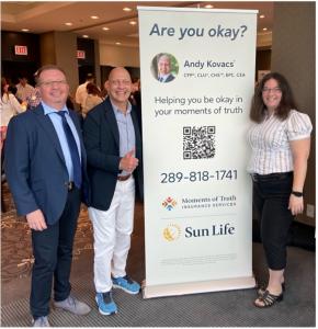 Andy Kovacs, President of Moments of Truth Insurance Services, stands together with Boriss Drujans of BD Real Estate Team and Lisa Mervin of L.J. Sales, in front of the Moments of Truth Insurance Services company banner at a Breakfast Networking event. Th