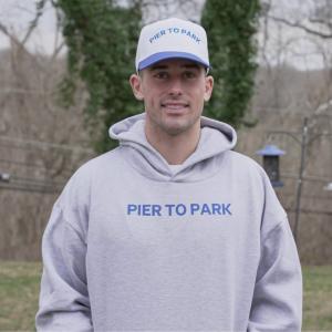 Andrew Linder stands in his yard wearing his Pier to Park sweatshirt and hat.