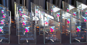 Alt text for Spectrum Award trophies: "An array of glass Spectrum Award trophies are displayed, featuring a transparent material with a reflective quality that catches the light. Each trophy has the AMA Phoenix logo, along with colorful Spectrum Logo grap