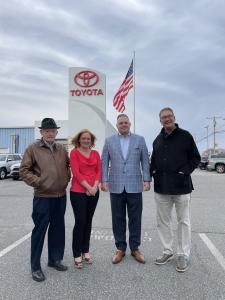 Bob Schwartz and Linda Schwartz with MJ Lofland and Charlie Burton of i.g. Burton Auto Group standing in dealer lot in front of American Flag